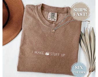 May include: A brown t-shirt with the text "I MAKE STUFF UP" printed in white. The shirt is made of a soft, comfortable material and has a relaxed fit.
