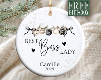 Puede incluir: Adorno navideño redondo de cerámica blanca con el texto «BEST Boss LADY Camille 2025». El adorno presenta un borde decorativo de bolas de Navidad y lazos. Se adjunta una cuerda dorada para colgarlo.