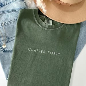 Pu&ograve; includere: Una maglietta verde con il testo "CHAPTER FORTY" in lettere bianche.