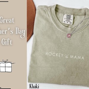 May include: Khaki green t-shirt with the text "HOCKEY MAMA" and a small pink tag with the text "COMFORT COLORS" on the front.