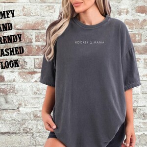 May include: A dark gray oversized t-shirt with the text "HOCKEY & MAMA" printed on the front. The shirt has a relaxed fit and a washed look.