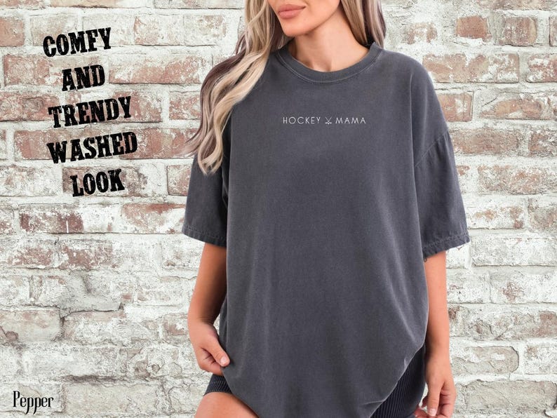 May include: A dark gray oversized t-shirt with the text "HOCKEY & MAMA" printed on the front. The shirt has a relaxed fit and a washed look.