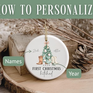 Op de afbeelding: Een witte keramische kerstbal met een kerstboomontwerp, cowboylaarzen en de tekst "First Christmas hitched" met het jaar 2025. De bal heeft een gouden touwtje om op te hangen. De tekst "How to Personalize" staat bovenaan.