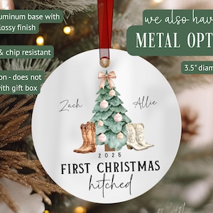 Op de afbeelding: Een witte, ronde kerstversiering met een rood lint. Het heeft een aquarelontwerp van een kerstboom, cowboylaarzen en de tekst "First Christmas hitched" met de namen "Zach" en "Allie" en het jaar 2025. De versiering heeft een diameter van 8,89 cm.