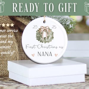 Puede incluir: Adorno navide&ntilde;o de cer&aacute;mica blanca con dise&ntilde;o de corona, el texto "First Christmas as NANA" y los a&ntilde;os 20 y 25. Las palabras "READY TO GIFT" est&aacute;n en la parte superior. El adorno est&aacute; sobre una caja blanca.