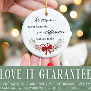 May include: A white ceramic ornament with the text "karen never forget the difference that you make." The ornament has a gold string for hanging and is decorated with a red bow and candy canes. The ornament is held in a person's hands.