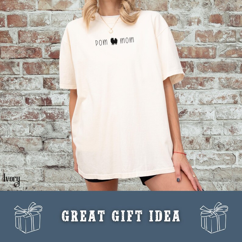 May include: Ivory-colored t-shirt with the text "POM MOM" and a silhouette of a dog. The shirt is a great gift idea. The shirt is made of a soft material.