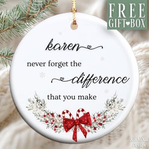May include: A white ceramic Christmas ornament with the text "Karen never forget the difference that you make." The ornament features a festive design with a red bow, candy canes, and greenery. A gold string is attached for hanging.