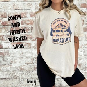 Puede incluir: Camiseta color marfil con un gr&aacute;fico de una autocaravana, monta&ntilde;as y las palabras "Explore Nature" y "Nomad Life". La camiseta tambi&eacute;n tiene las palabras "Comfy and Trendy Washed Look" impresas en el lado izquierdo. La palabra "Ivory" est&aacute; impresa en la parte inferior.