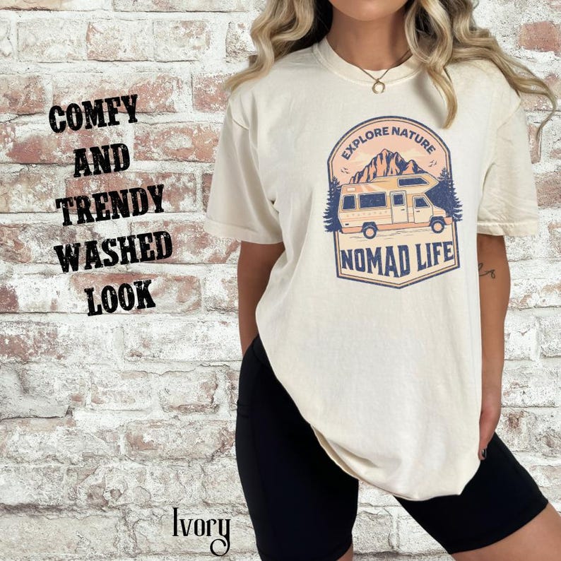Puede incluir: Camiseta color marfil con un gr&aacute;fico de una autocaravana, monta&ntilde;as y las palabras "Explore Nature" y "Nomad Life". La camiseta tambi&eacute;n tiene las palabras "Comfy and Trendy Washed Look" impresas en el lado izquierdo. La palabra "Ivory" est&aacute; impresa en la parte inferior.
