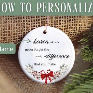 May include: A white ceramic ornament with a gold string for hanging. The ornament has the text "Karen, never forget the difference that you make." A red bow and candy canes decorate the bottom. The background includes a Christmas tree and burlap.