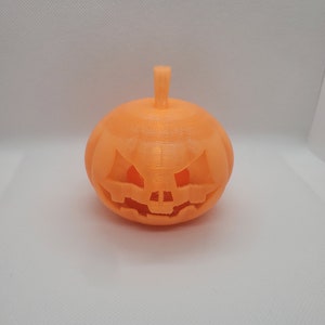 Può includere: Una zucca arancione stampata in 3D con un viso di zucca intagliato.