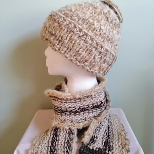 May include: A beige and brown knitted hat and scarf set. The hat has a pompom on top and the scarf has a striped pattern.