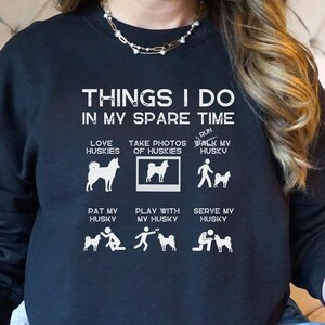 Könnte beinhalten: Schwarzes Sweatshirt mit weißem Text, der "Things I do in my spare time" lautet. Der Text wird von einer Liste von Aktivitäten gefolgt, die mit Huskys zu tun haben, darunter "Love Huskies", "Take Photos of Huskies", "Walk My Husky", "Pat My Husky", "Play With My Husky" und "Serve My Husky". Jede Aktivität wird mit einer kleinen Grafik eines Huskys illustriert.