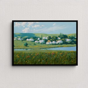 May include: A framed landscape painting depicts a serene rural scene. A body of water reflects the sky, with a field of wildflowers in the foreground. Rolling green hills and white-blossomed trees dot the background under a blue sky with fluffy clouds.