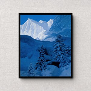 May include: A framed print of a snow-covered mountain range. The artwork features a blue and white color palette, with snow-covered evergreen trees in the foreground. The sky is a clear blue.