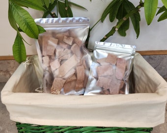 May include: Two clear plastic bags filled with brown, dried meat treats. The bags are sitting in a light brown wicker basket with a green liner.