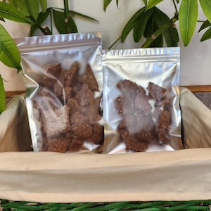 May include: Two clear plastic bags filled with small, irregularly shaped, dark brown pieces of food. The bags are sitting in a light brown wicker basket.