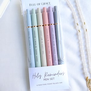 Holy Reminders Catholic Pen Set packaged in clear sleeve with Full of Grace Studio branding, featuring six pastel engraved pens with inspirational faith messages.