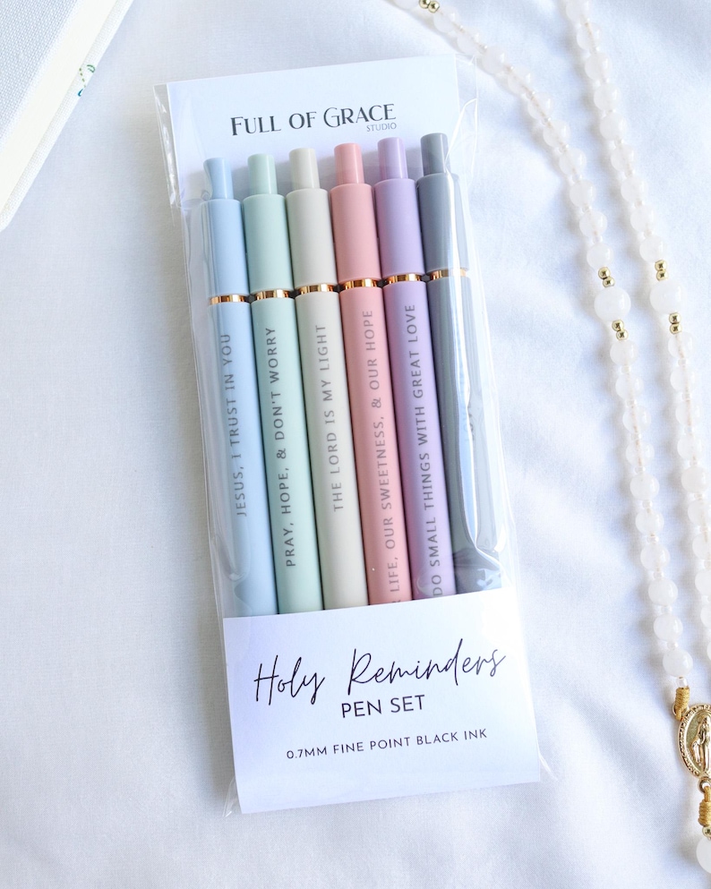 Holy Reminders Catholic Pen Set packaged in clear sleeve with Full of Grace Studio branding, featuring six pastel engraved pens with inspirational faith messages.