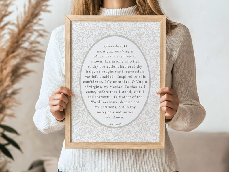 Woman holding a framed Memorare Prayer printable wall art with beige floral background — minimalist Catholic digital download artwork featuring Marian devotion for faith-filled homes.