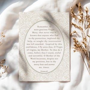 Memorare Prayer printable Catholic art card lying on soft white fabric with dried florals — vintage-style Marian devotion wall art digital download for Catholic home decor.