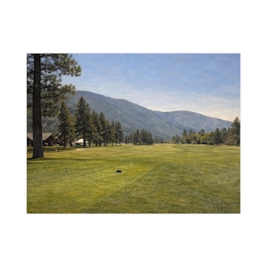 May include: A picturesque golf course scene under a bright sky. The image shows a wide green fairway, bordered by trees, with mountains in the distance. The sky is a clear blue, creating a serene atmosphere.