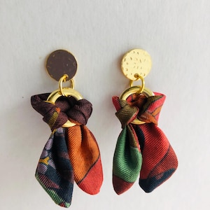 以下が含まれることがあります： 赤、緑、茶色、オレンジの色合いで結ばれた布のボウが付いたゴールドトーンのイヤリングのペア。布はペイズリー柄です。