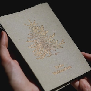 Könnte beinhalten: Eine rechteckige Grußkarte aus strukturiertem, hellbraunem Papier mit Büttenrand. Die Karte zeigt eine Illustration eines stilisierten Tannenbaums in metallischer Goldfolie und den geprägten goldenen Schriftzug Frohe Weihnachten.