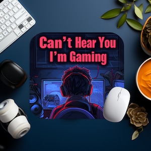 May include: A black and blue gaming mouse mat with a gamer sitting in front of a computer screen. The text on the mouse mat reads "Can't Hear You I'm Gaming".