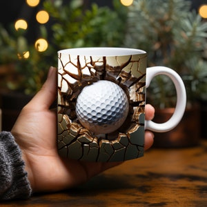 May include: White ceramic mug with a golf ball breaking through a cracked gold surface. The mug has a white handle.