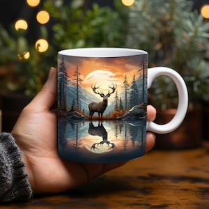 May include: White ceramic mug featuring a scenic landscape with a deer standing in a lake, reflecting the image of the deer and the surrounding forest and mountains. The background shows a sunset with orange and yellow hues.