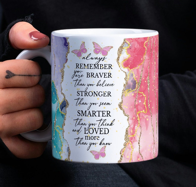 May include: White ceramic mug with a pink and blue watercolor design and gold glitter. The mug has a quote that reads "always remember you are braver than you believe stronger than you seem smarter than you think and loved more than you know".