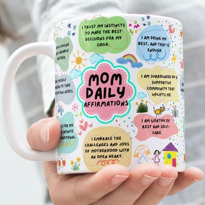 Op de afbeelding: Witte keramische mok met de tekst "Mom Daily Affirmations" in een roze wolkontwerp. De mok is versierd met kleurrijke affirmaties, waaronder "I am worthy of rest and self-care."