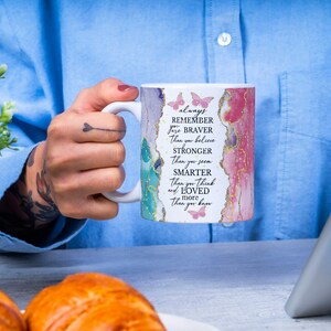 May include: White ceramic mug with a pink and blue watercolor design and gold accents. The mug has a quote that reads "always remember you are braver than you believe stronger than you seem smarter than you think and loved more than you know".