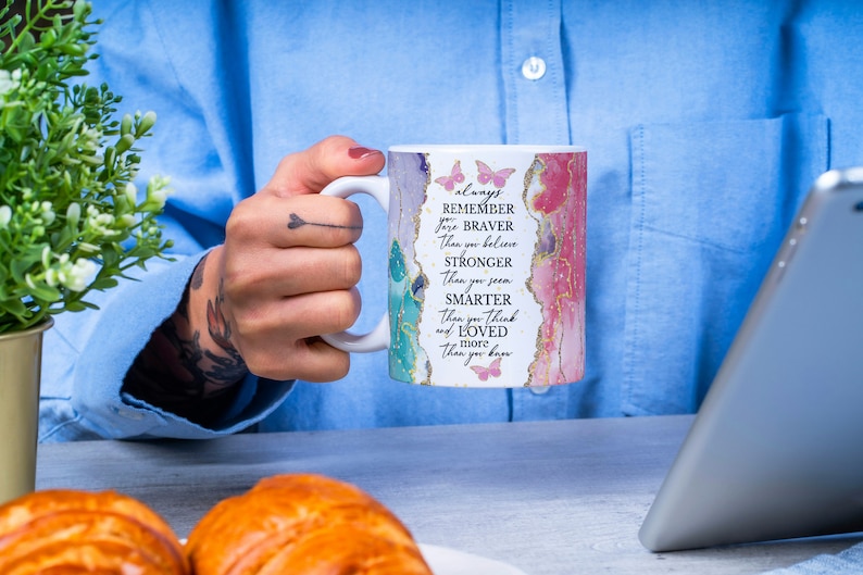 May include: White ceramic mug with a pink and blue watercolor design and gold accents. The mug has a quote that reads "always remember you are braver than you believe stronger than you seem smarter than you think and loved more than you know".