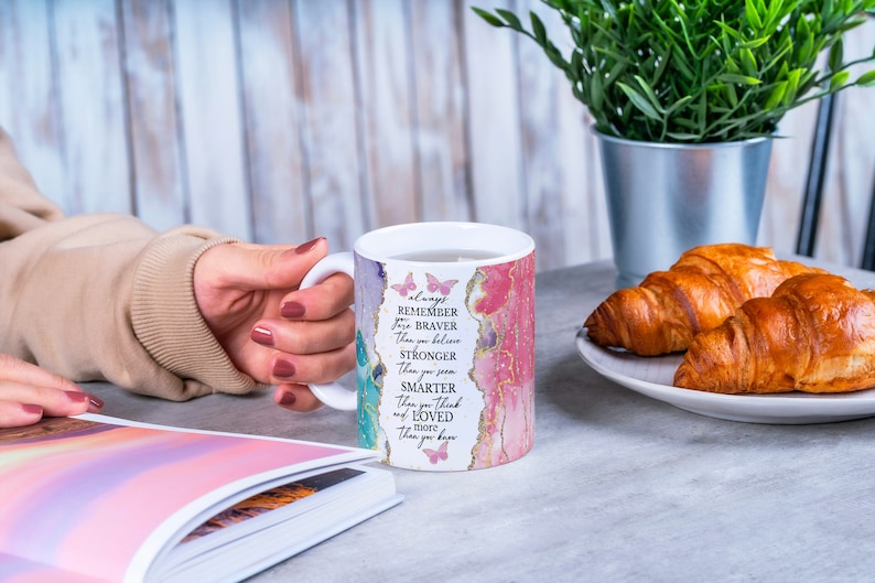 May include: White ceramic mug with a pink, green, and gold watercolor design and the text "always remember you are braver than you believe stronger than you seem smarter than you think and more loved than you know".
