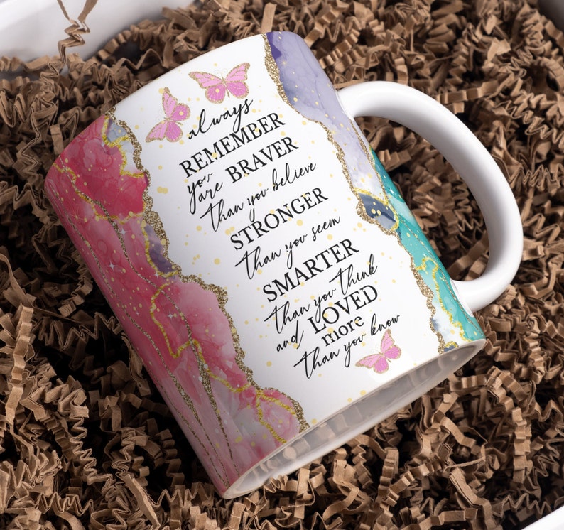 May include: White ceramic mug with a pink, blue, and green marble design and gold glitter accents. The mug has a handle and features the text "always remember you are braver than you believe stronger than you seem smarter than you think and loved more than you know".