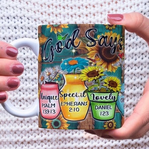 Op de afbeelding: Witte keramische mok met een kleurrijk ontwerp met zonnebloemen, vlinders en de tekst "God Says" met drie bloempotten waarop "Unique", "Special" en "Lovely" staat met bijbelteksten.