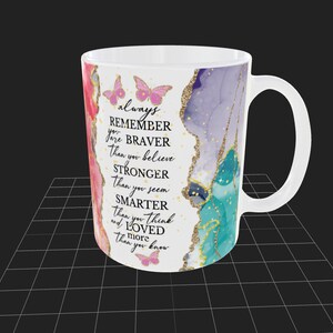 May include: White ceramic mug with a colorful abstract design and gold glitter accents. The mug features a motivational quote: "always REMEMBER you are BRAVER than you believe STRONGER than you seem SMARTER than you think and LOVED more than you know".