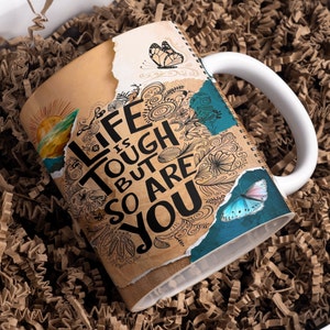 May include: White ceramic mug with a brown and blue design. The mug has a quote that reads "Life is tough but so are you".
