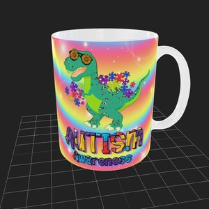 Puede incluir: Una taza de cer&aacute;mica blanca con un fondo de arco&iacute;ris colorido y un dinosaurio verde con gafas de sol. El dinosaurio sostiene piezas de rompecabezas y el texto "Autism Awareness" est&aacute; impreso debajo del dinosaurio.