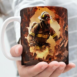 May include: White ceramic coffee mug with a graphic of a firefighter breaking through a wall of flames. The firefighter is wearing a helmet, a yellow and black uniform, and a breathing apparatus.