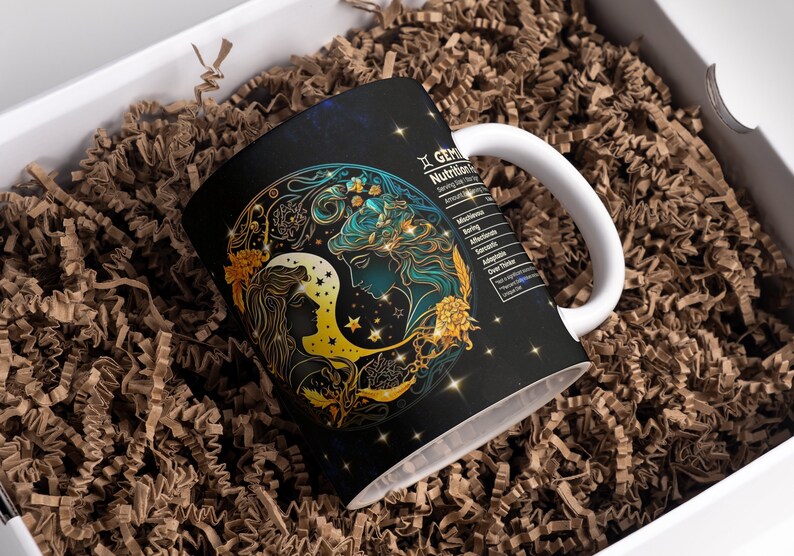 May include: A white ceramic mug with a black background and a gold and blue illustration of the Gemini zodiac sign. The mug has a handle and the text "Gemini Nutrition Facts" is printed on the side.
