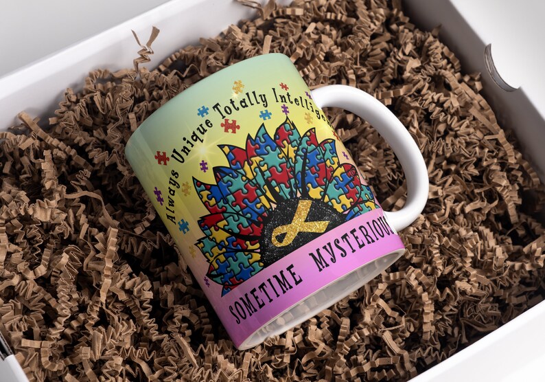 Puede incluir: Una taza de cer&aacute;mica blanca con un dise&ntilde;o colorido que presenta un girasol hecho de piezas de rompecabezas. El texto "Always Unique Totally Intelligent Sometime Mysterious" est&aacute; impreso en la taza.