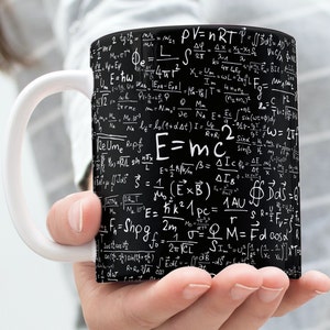 Könnte beinhalten: Eine Kaffeetasse mit weißem Griff und schwarzer Außenseite, die mit weißen mathematischen Formeln und Gleichungen bedeckt ist. Die Tasse zeigt die Gleichung E=mc² prominent. Ein perfektes Geschenk für Wissenschaftsbegeisterte.