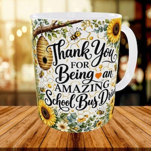 Op de afbeelding: Een witte keramische mok met een grafische print van zonnebloemen, honingbijen en een bijenkorf. De tekst luidt, Thank You FOR Being an AMAZING School Bus Driver, met een oranje hartje. Het ontwerp bevat een geel honingraatpatroon.