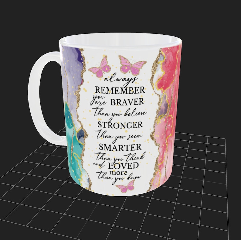 May include: White ceramic mug with a pink, purple, and blue watercolor design. The mug has gold glitter accents and butterflies. The text on the mug reads: "always remember you are braver than you believe stronger than you seem smarter than you think and loved more than you know."
