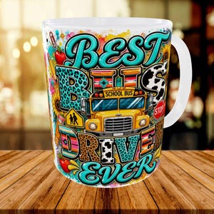 May include: A white ceramic mug featuring a colorful graphic design with a yellow school bus, sunflowers, apples, and pencils. The text reads BEST BUS DRIVER EVER in bold teal lettering, accented with leopard print, cow print, and striped patterns.