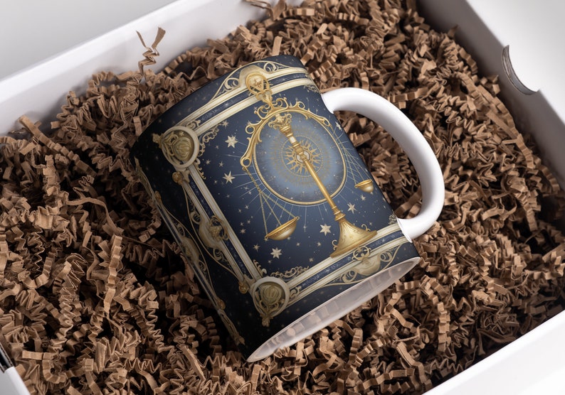 May include: A white ceramic mug with a blue and gold design featuring a zodiac scale symbol. The mug is in a white box with brown packing paper.